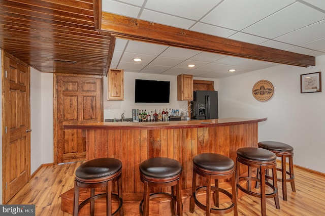 bar featuring light hardwood / wood-style flooring, a drop ceiling, and black refrigerator with ice dispenser