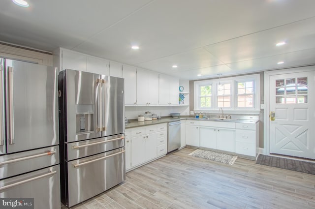 kitchen with light wood finished floors, white cabinets, stainless steel appliances, light countertops, and a sink