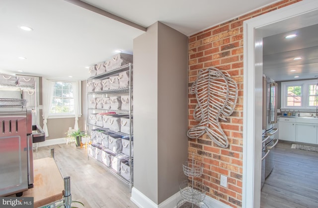 hall featuring brick wall, baseboards, a healthy amount of sunlight, and light wood finished floors