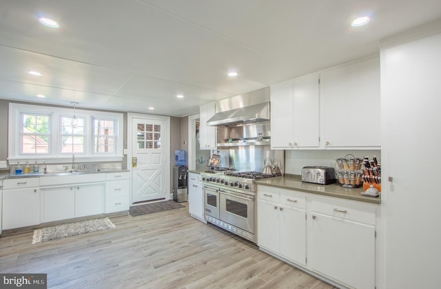 kitchen with wall chimney exhaust hood, range with two ovens, dark countertops, and white cabinetry