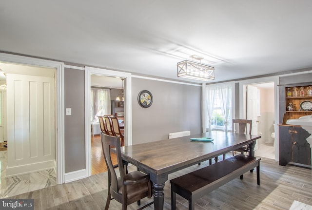 dining area featuring baseboards, radiator heating unit, light wood-style flooring, and a notable chandelier