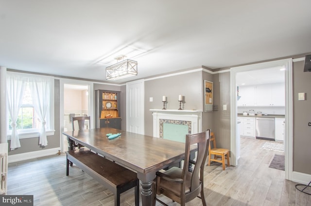 dining area with light wood-style floors, crown molding, a fireplace, and baseboards