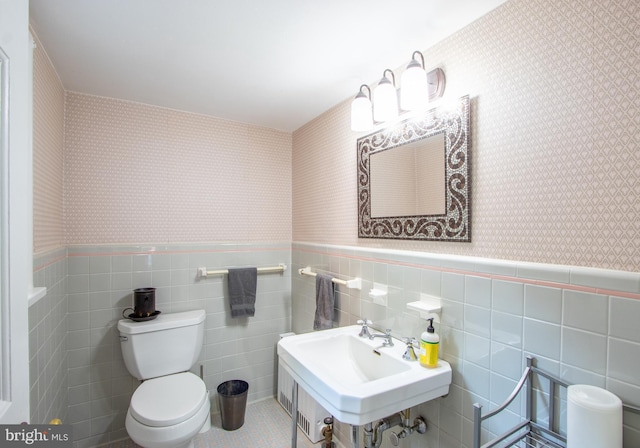 half bathroom with toilet, wallpapered walls, and a wainscoted wall