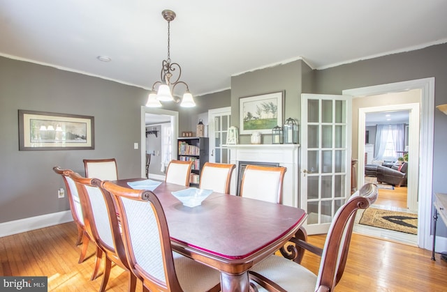 dining space featuring light wood-style floors, a fireplace, ornamental molding, and baseboards