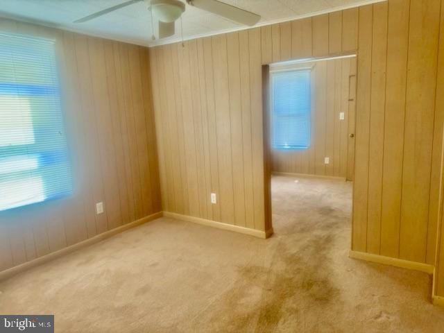 carpeted empty room featuring a wealth of natural light, wooden walls, and ceiling fan