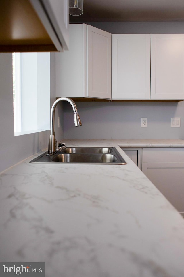 kitchen with light stone counters, sink, and white cabinetry