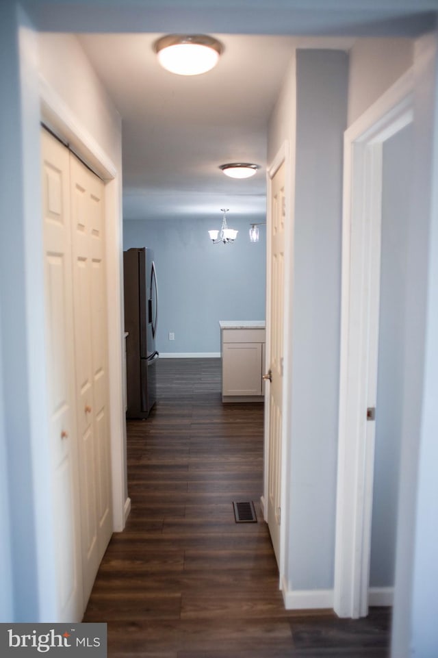 corridor with dark hardwood / wood-style flooring and a notable chandelier