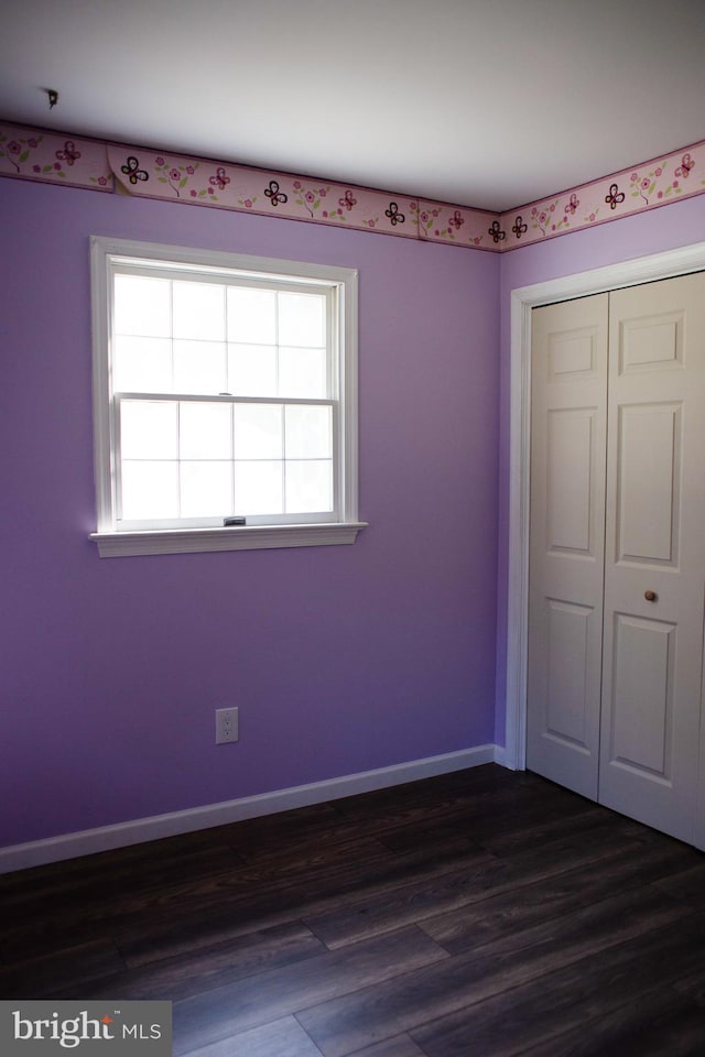 unfurnished bedroom featuring dark hardwood / wood-style flooring, a closet, and multiple windows