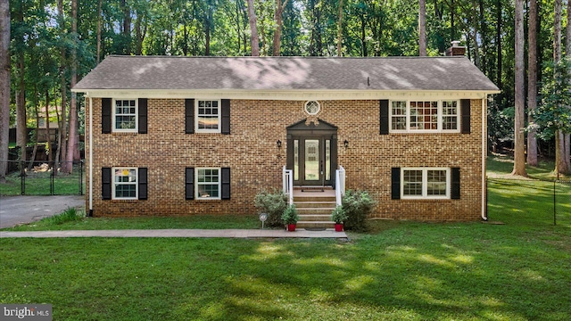 bi-level home featuring brick siding, a chimney, a front yard, fence, and driveway