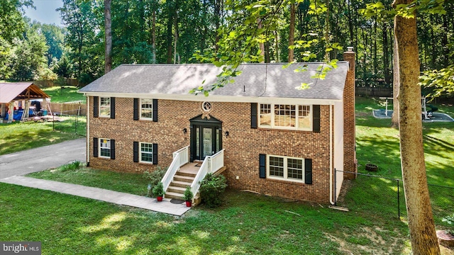 raised ranch with brick siding, a chimney, a front yard, fence, and driveway