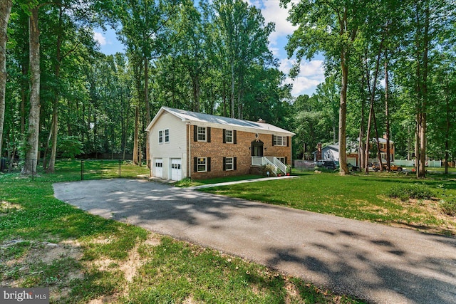 raised ranch with an attached garage, driveway, a front lawn, and brick siding