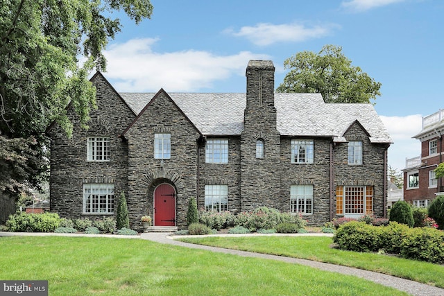 view of front of property with stone siding, a high end roof, a chimney, and a front yard