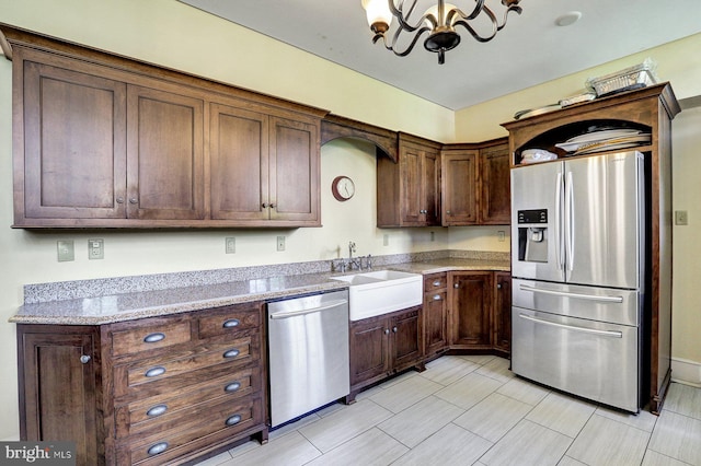 kitchen with appliances with stainless steel finishes, an inviting chandelier, light stone countertops, dark brown cabinetry, and sink