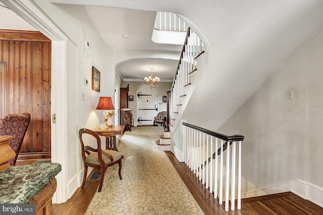 corridor with a notable chandelier, wood-type flooring, and ornamental molding