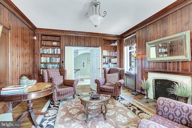 sitting room featuring ornamental molding, light hardwood / wood-style flooring, built in shelves, and wood walls