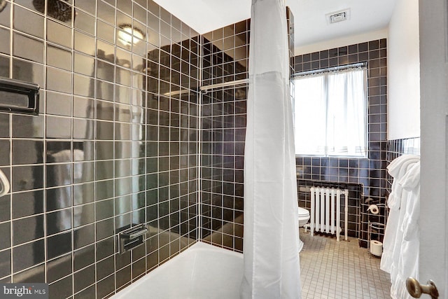 bathroom with radiator heating unit, toilet, tile patterned floors, shower / bath combo with shower curtain, and tile walls