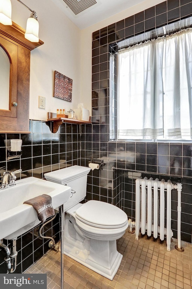 bathroom featuring toilet, radiator heating unit, tile patterned floors, and tile walls