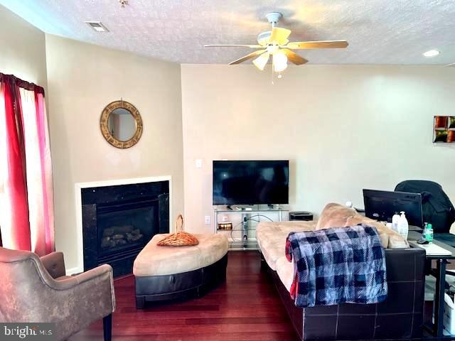 living room with ceiling fan, dark hardwood / wood-style floors, and a textured ceiling