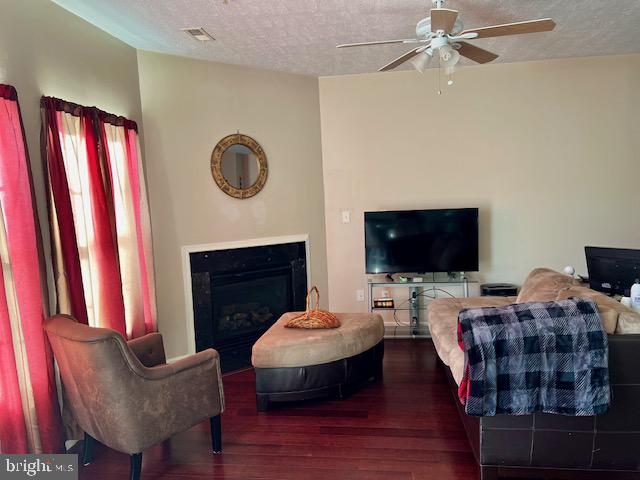 living room with ceiling fan, a textured ceiling, and dark wood-type flooring