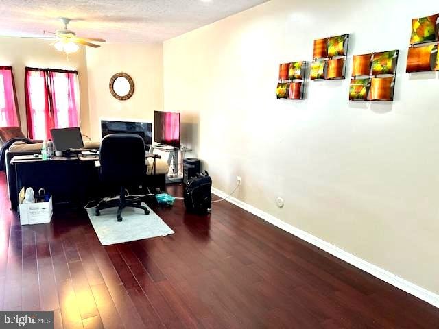 home office featuring a textured ceiling, dark hardwood / wood-style flooring, and ceiling fan