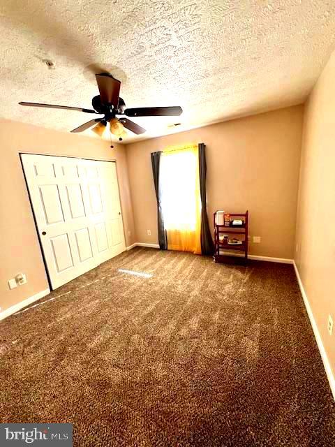 unfurnished bedroom featuring ceiling fan, a textured ceiling, a closet, and dark colored carpet