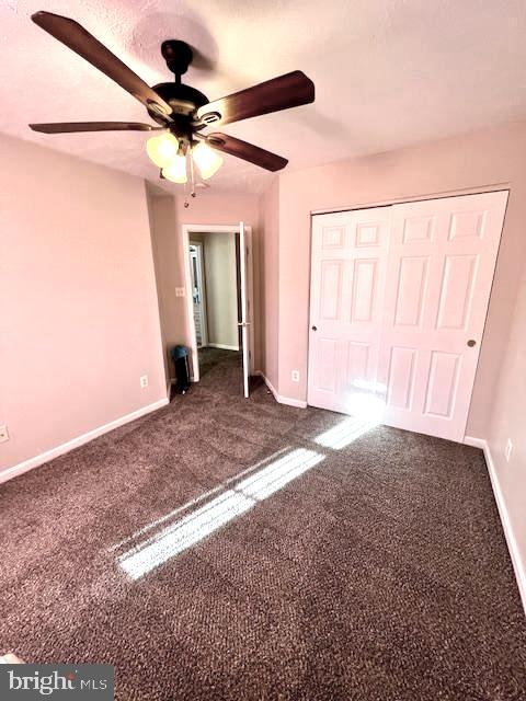 unfurnished bedroom with ceiling fan, a closet, and dark carpet