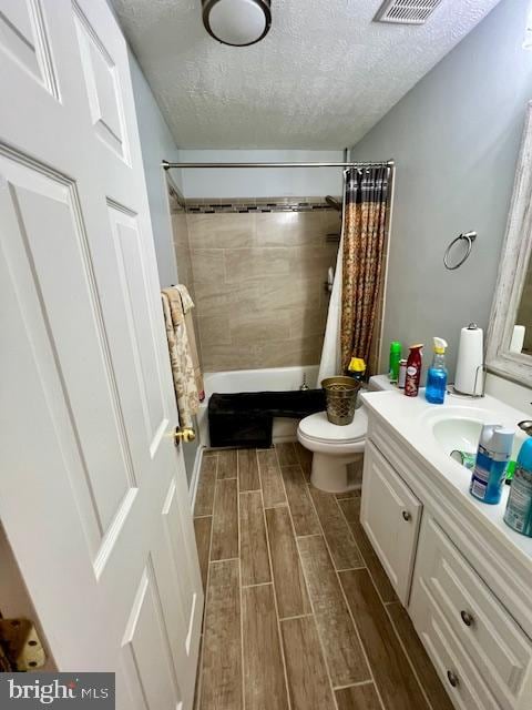 full bathroom with vanity, a textured ceiling, shower / bath combo with shower curtain, hardwood / wood-style flooring, and toilet