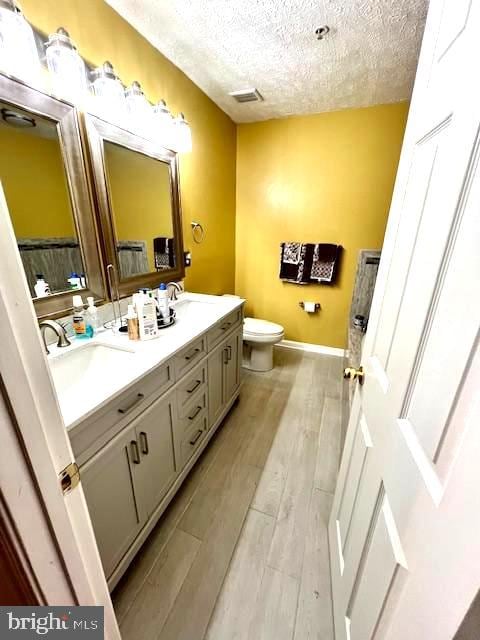 bathroom featuring vanity, hardwood / wood-style floors, toilet, and a textured ceiling