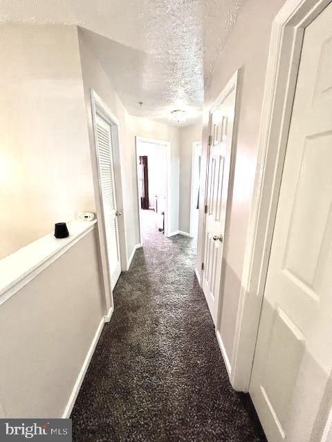 corridor with a textured ceiling and dark carpet