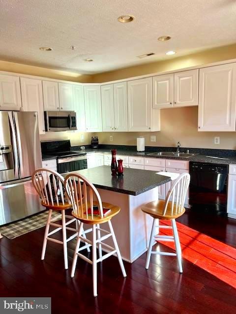 kitchen featuring a breakfast bar, dark wood-type flooring, white cabinetry, and black appliances