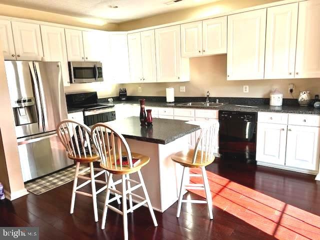 kitchen featuring white cabinets, a kitchen island, dark wood-type flooring, and black appliances