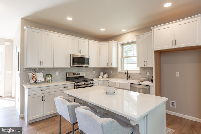 kitchen featuring backsplash, appliances with stainless steel finishes, light hardwood / wood-style flooring, and white cabinetry