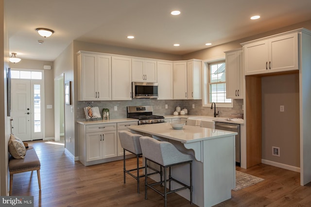 kitchen featuring a kitchen island, hardwood / wood-style floors, white cabinets, appliances with stainless steel finishes, and tasteful backsplash