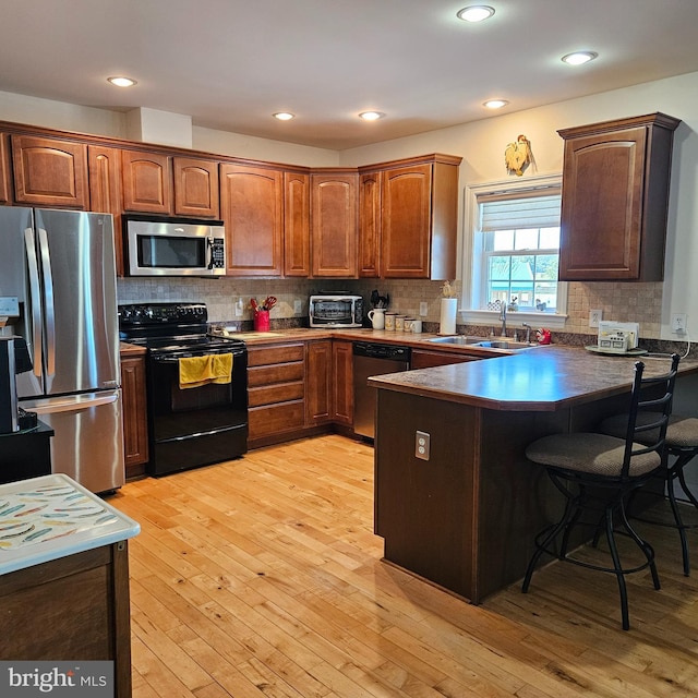 kitchen with appliances with stainless steel finishes, a breakfast bar, backsplash, light wood-type flooring, and sink