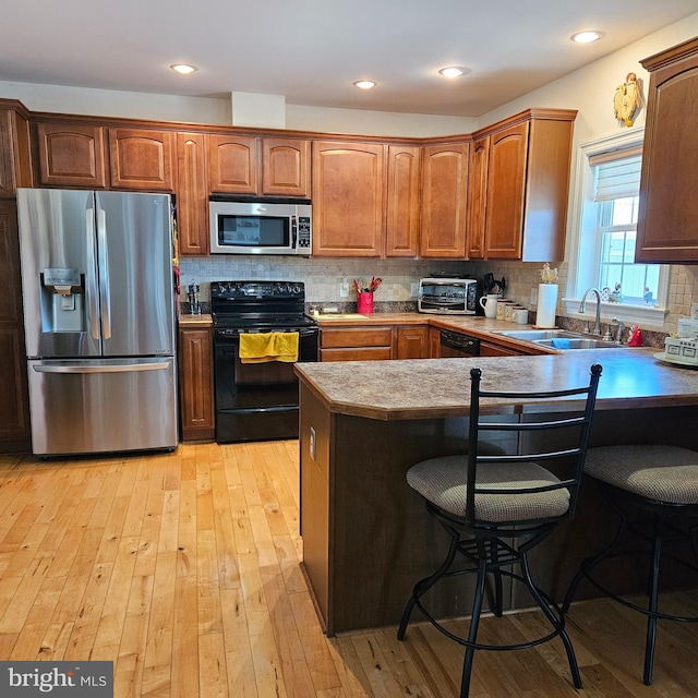 kitchen with a breakfast bar, sink, kitchen peninsula, light hardwood / wood-style flooring, and stainless steel appliances