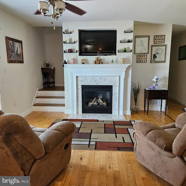 living room with light wood-type flooring, a high end fireplace, and ceiling fan