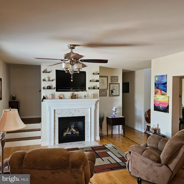 living room featuring a premium fireplace, ceiling fan, and light hardwood / wood-style flooring