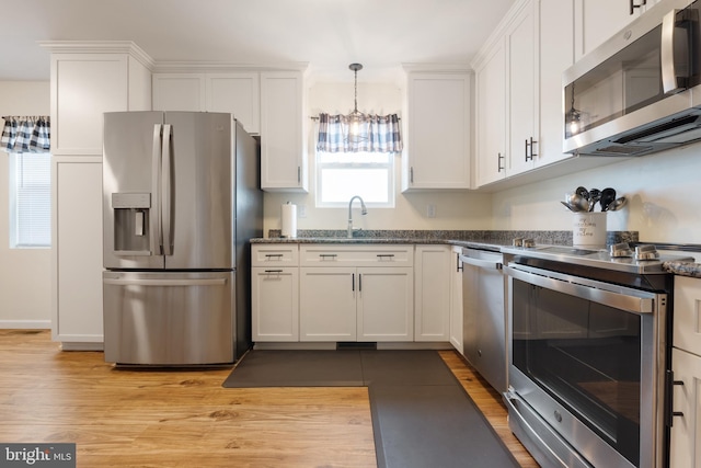 kitchen featuring light wood-type flooring, pendant lighting, stainless steel appliances, and white cabinets