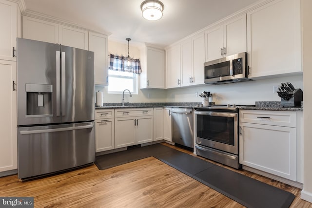 kitchen featuring light wood-type flooring, appliances with stainless steel finishes, white cabinetry, sink, and dark stone counters