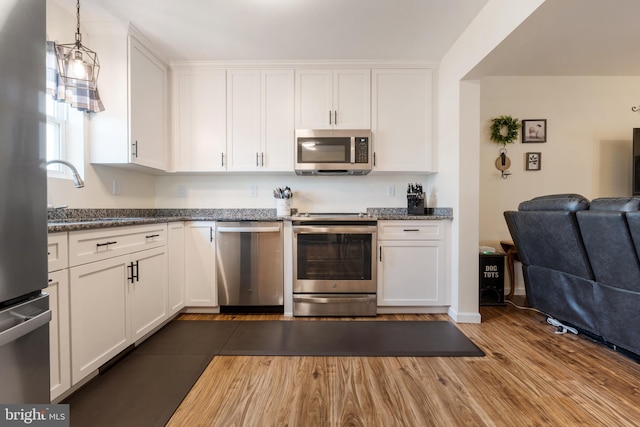 kitchen featuring dark stone counters, hardwood / wood-style floors, white cabinetry, stainless steel appliances, and sink