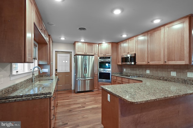 kitchen with stainless steel appliances, light hardwood / wood-style floors, tasteful backsplash, sink, and light stone counters