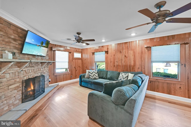 living room with ceiling fan, wooden walls, light wood-type flooring, and a stone fireplace