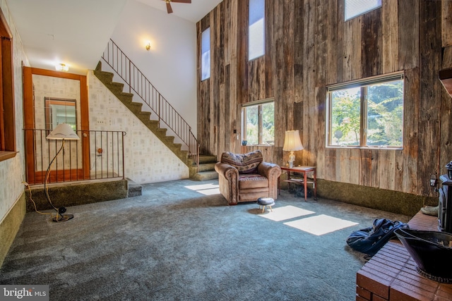 unfurnished room featuring stairs, wooden walls, a high ceiling, and carpet floors