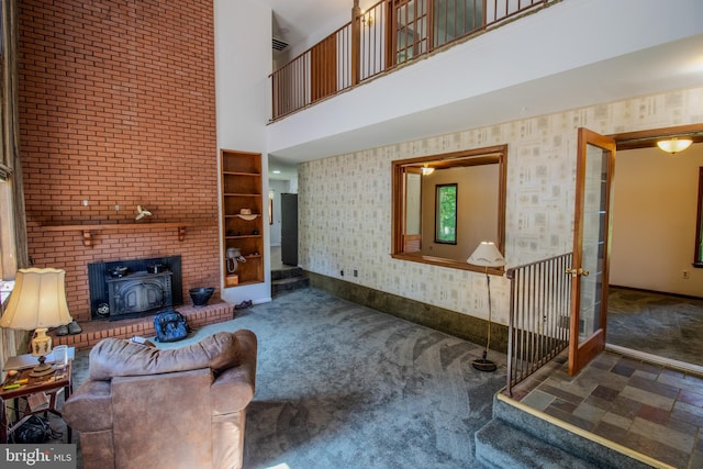 living room with wallpapered walls, baseboards, carpet flooring, a wood stove, and a towering ceiling