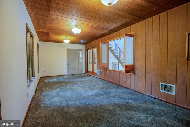 carpeted spare room with visible vents, wood walls, and wooden ceiling