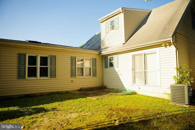 rear view of property with central air condition unit, roof with shingles, and a yard