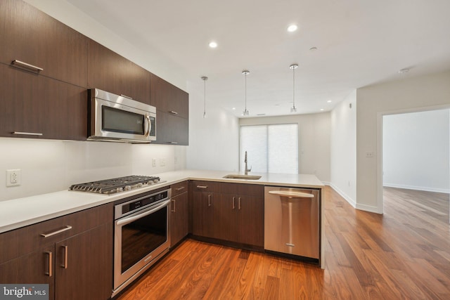 kitchen with kitchen peninsula, pendant lighting, stainless steel appliances, dark hardwood / wood-style floors, and sink