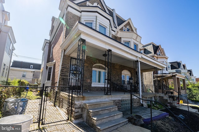 view of front of house featuring fence, a porch, brick siding, and a gate