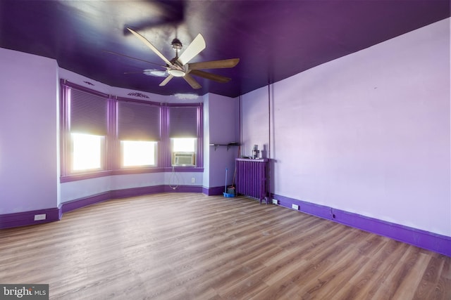 empty room featuring ceiling fan, baseboards, radiator heating unit, cooling unit, and wood finished floors