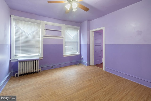 empty room with radiator, wood finished floors, baseboards, and ceiling fan